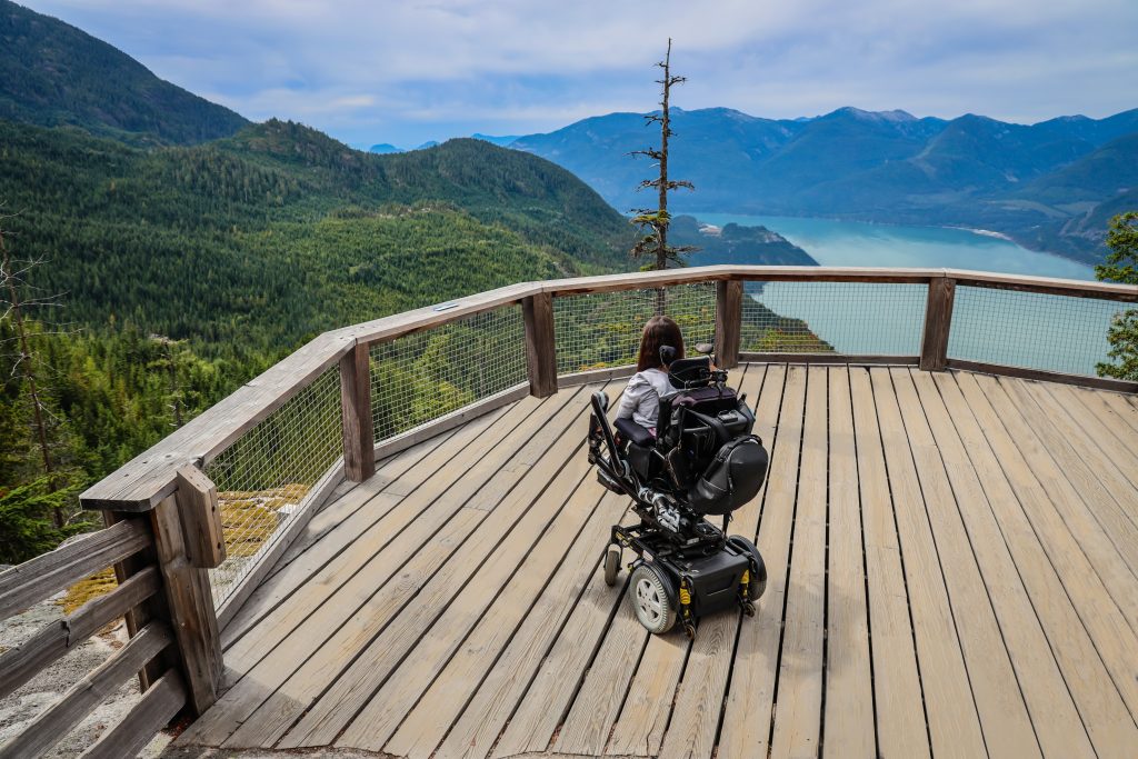 Tori in her motorized wheelchair, looking out at the view on the viewing platform at the sea to sky gondola in Squamish British Columbia