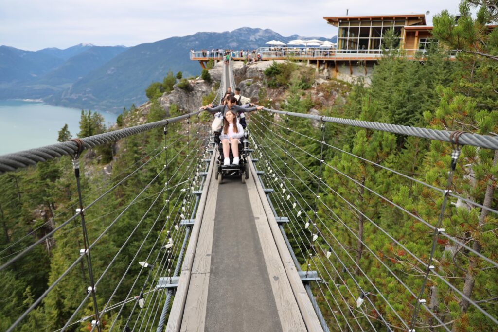 Tori driving across the sky pilot suspension bridge in her motorized wheelchair. 