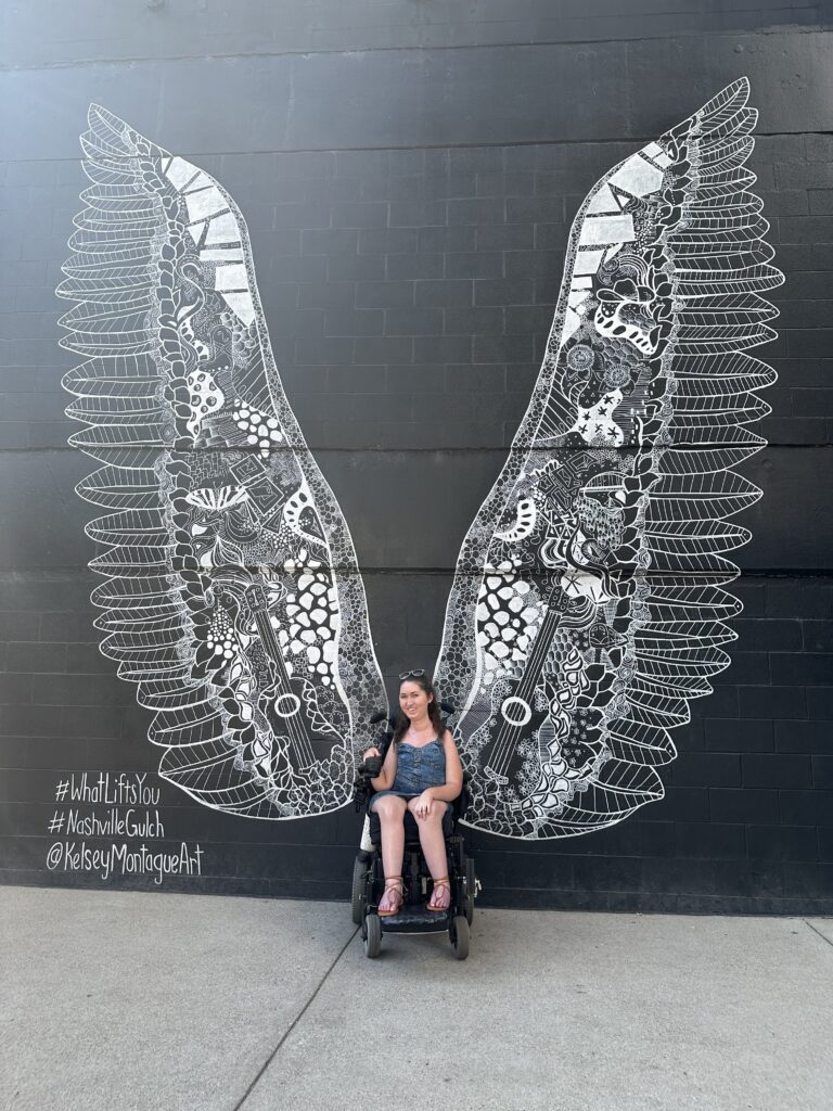 Wheelchair accessible travel blogger, Tori Hunter, sitting in her wheelchair in front of the "What Lifts You" wings mural located in the Gultch in Nashville Tennessee