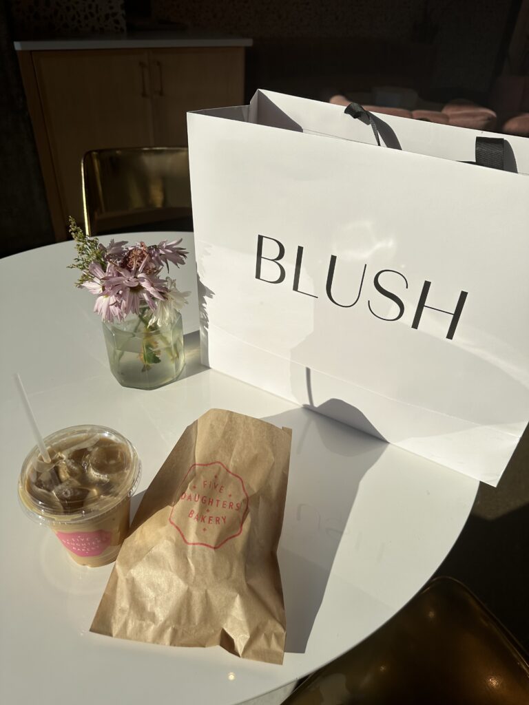 Iced coffee and a bag with a sweet treat in it from Five Daughters's bakery in Nashville. Beside it, there is a shopping bag from blush