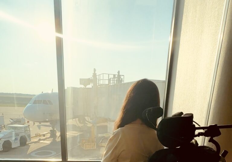 Tori Hunter, a disabled travel blogger, sitting in her wheelchair at an airport watching the planes get ready for takeoff