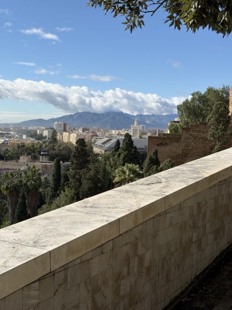 Panoramic view of Malaga city and the surrounding mountains seen from the wheelchair accessible terrace of Alcazaba fortress in Malaga, Spain, with lush gardens and palm trees below