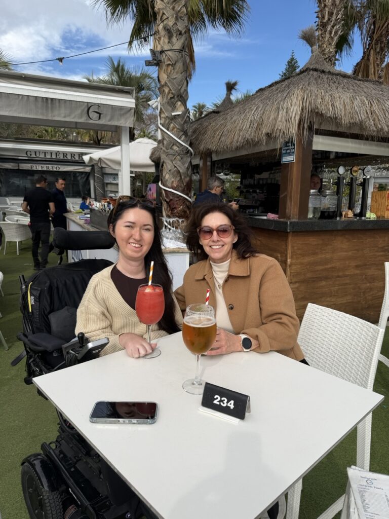 Tori Hunter, a wheelchair accessible travel blogger, and her companion enjoying drinks at the outdoor terrace of Gutierrez Puerto restaurant at the port of Malaga, Spain — a wheelchair accessible waterfront restaurant in Malaga
