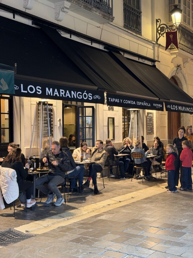 The busy outdoor terrace of Los Marangós tapas restaurant in Malaga, Spain at night, with diners seated at tables along a pedestrian street — a wheelchair accessible tapas restaurant in Malaga city centre