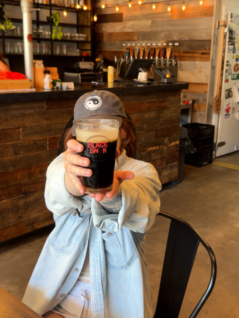 A pint of dark craft beer in a Black Swan Brewery glass, showing Stratford, Ontario branding, at the accessible brewery taproom in downtown Stratford
