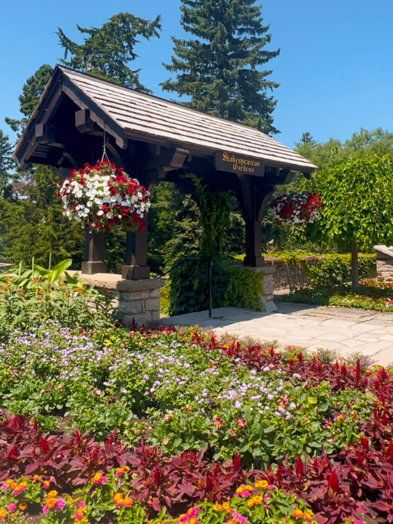 The wooden entrance gazebo and hanging flower baskets marking the entrance to Shakespearean Gardens in Stratford, Ontario
