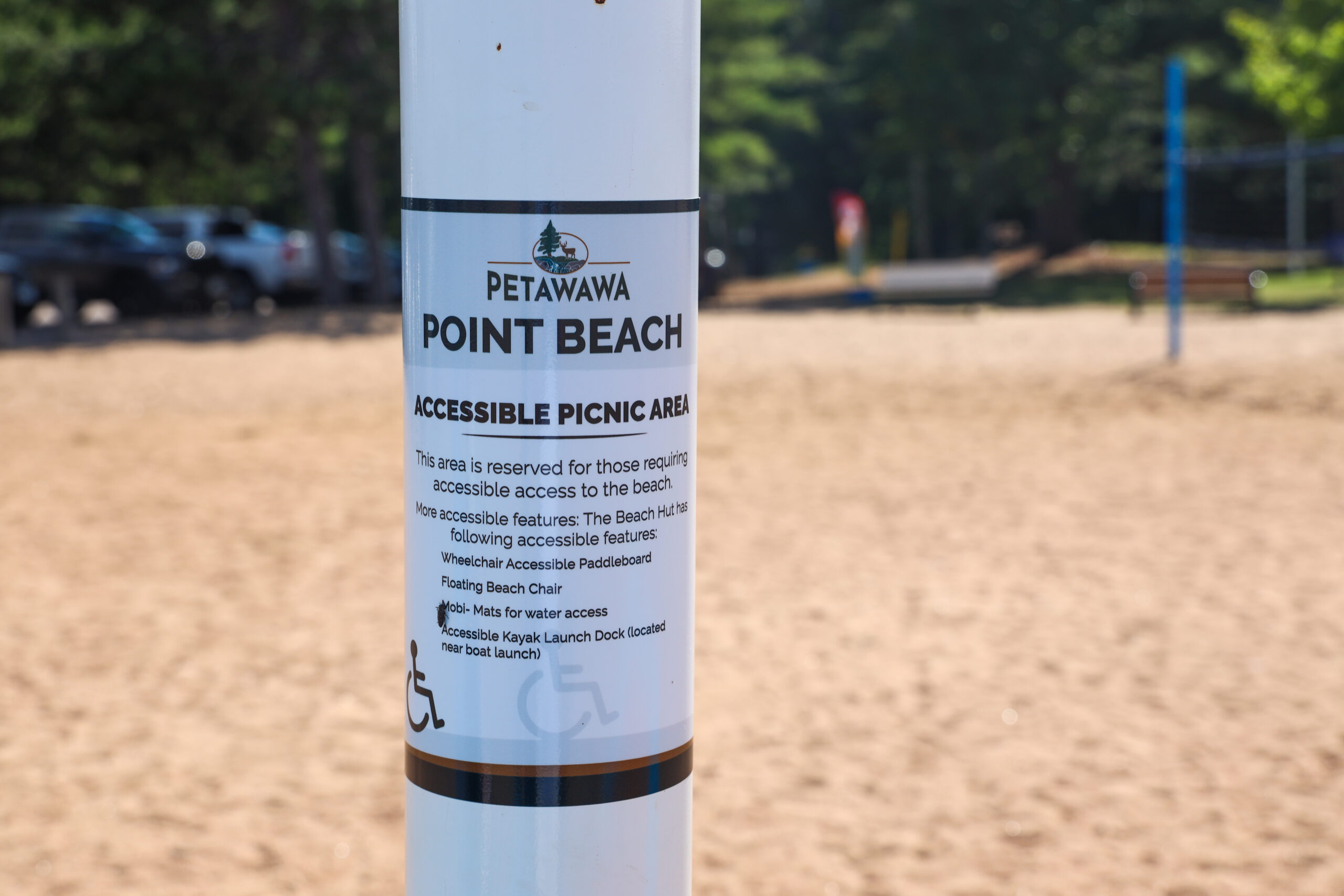 An accessible picnic area sign at Petawawa Point Beach in Ontario listing the wheelchair accessible paddleboard, floating beach chair, Mobi-Mats, and accessible kayak launch dock available at the beach.