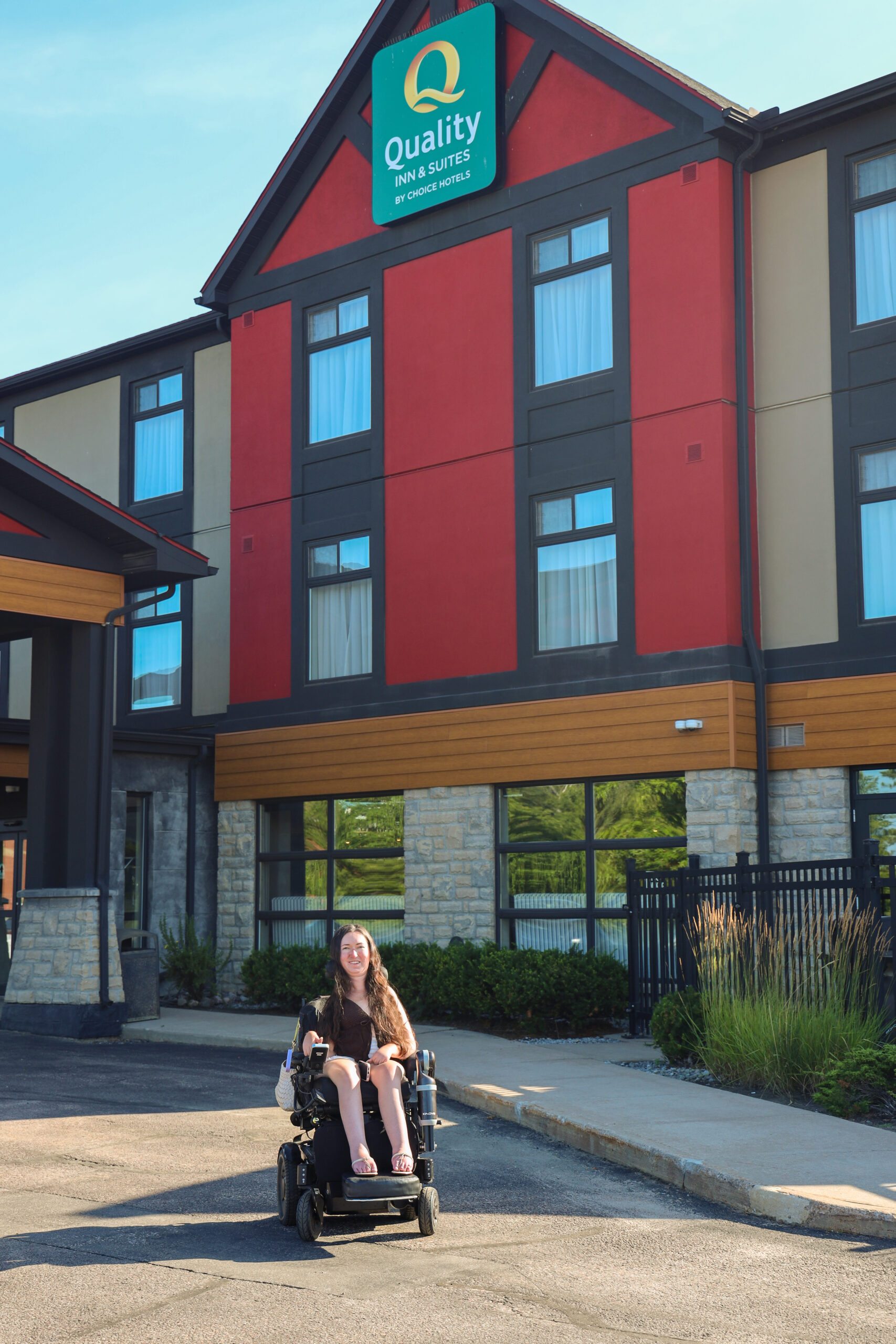 Tori Hunter, a wheelchair user and disabled travel blogger, in her power wheelchair outside the barrier-free entrance of the Quality Inn & Suites, a wheelchair accessible hotel in Petawawa, Ontario.