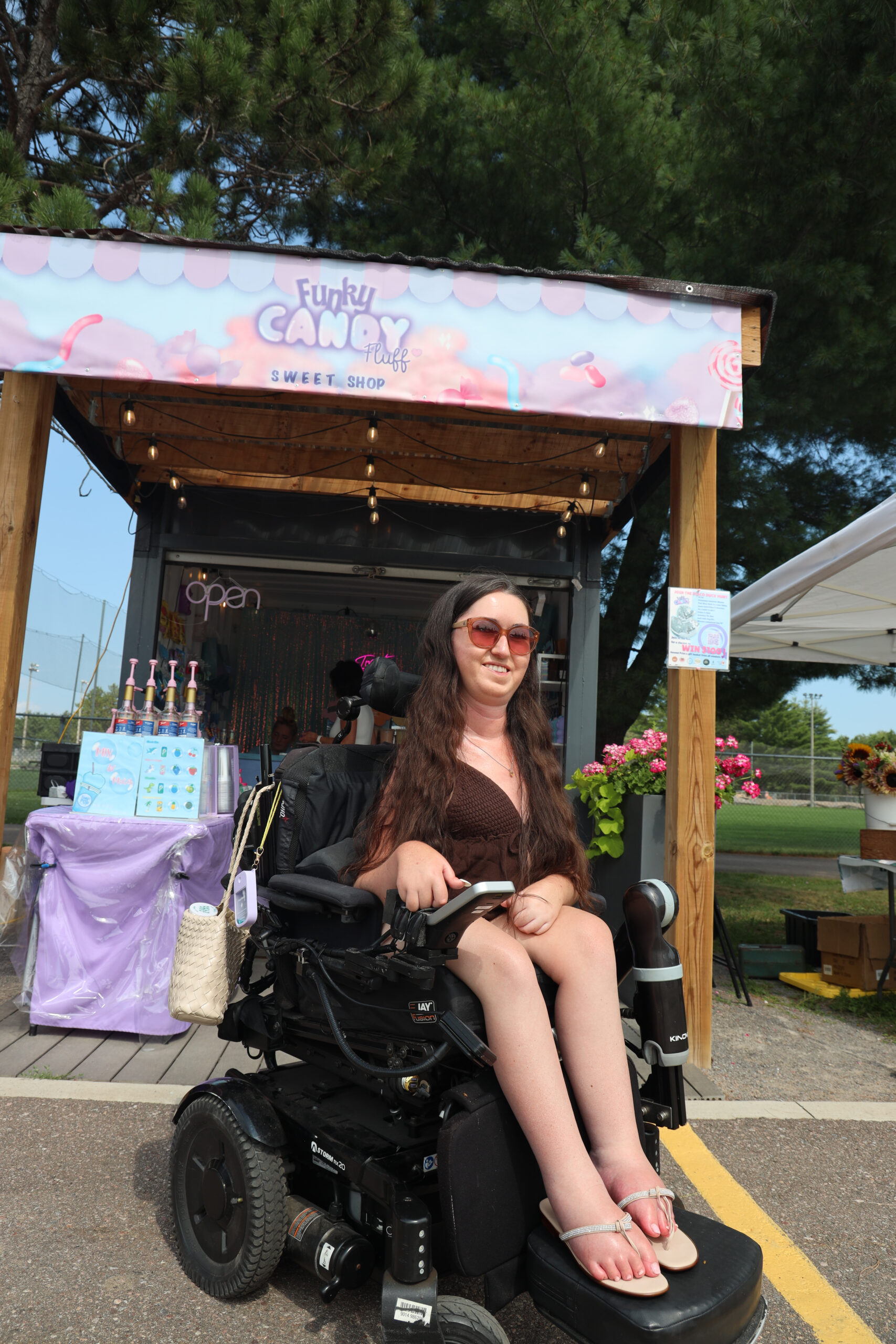 Tori Hunter, a wheelchair user and disabled travel blogger, in her power wheelchair outside the Funky Candy Fluff Sweet Shop, a shipping-container candy stand at the Container Market in Petawawa, Ontario.