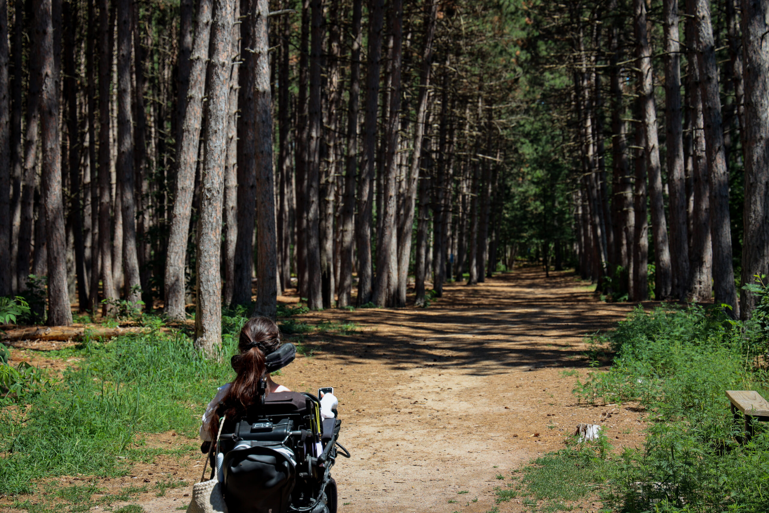Tori Hunter, a wheelchair user and disabled travel blogger, rolling her power wheelchair along the sandy, tree-lined Aki Trail at Petawawa Terrace Provincial Park in Ontario.