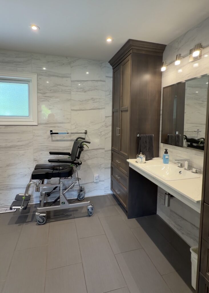 Spacious wheelchair accessible bathroom at Country Oasis Accessible Retreat in Innerkip, Ontario, with a roll-under sink, a tilting shower commode chair and a step-free tiled floor