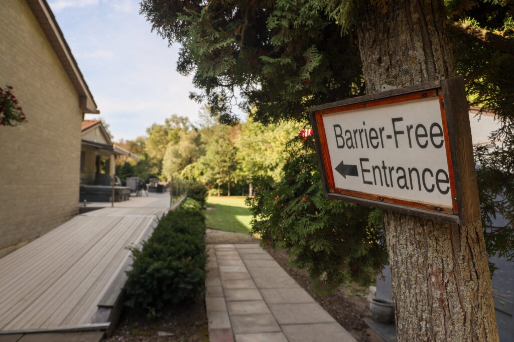 Sign pointing to the barrier-free entrance beside a wide wooden ramp and paved path at Country Oasis Accessible Retreat, a wheelchair accessible Airbnb in Innerkip, Oxford County, Ontario