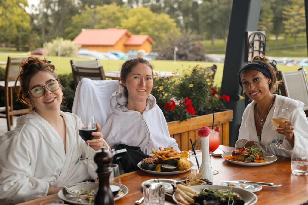 Tori Hunter, a wheelchair user and disabled travel blogger, and two friends in spa robes sharing dinner, wine and cocktails on the patio at KALOS restaurant at The Oxford Hills in Mount Elgin, Oxford County, Ontario